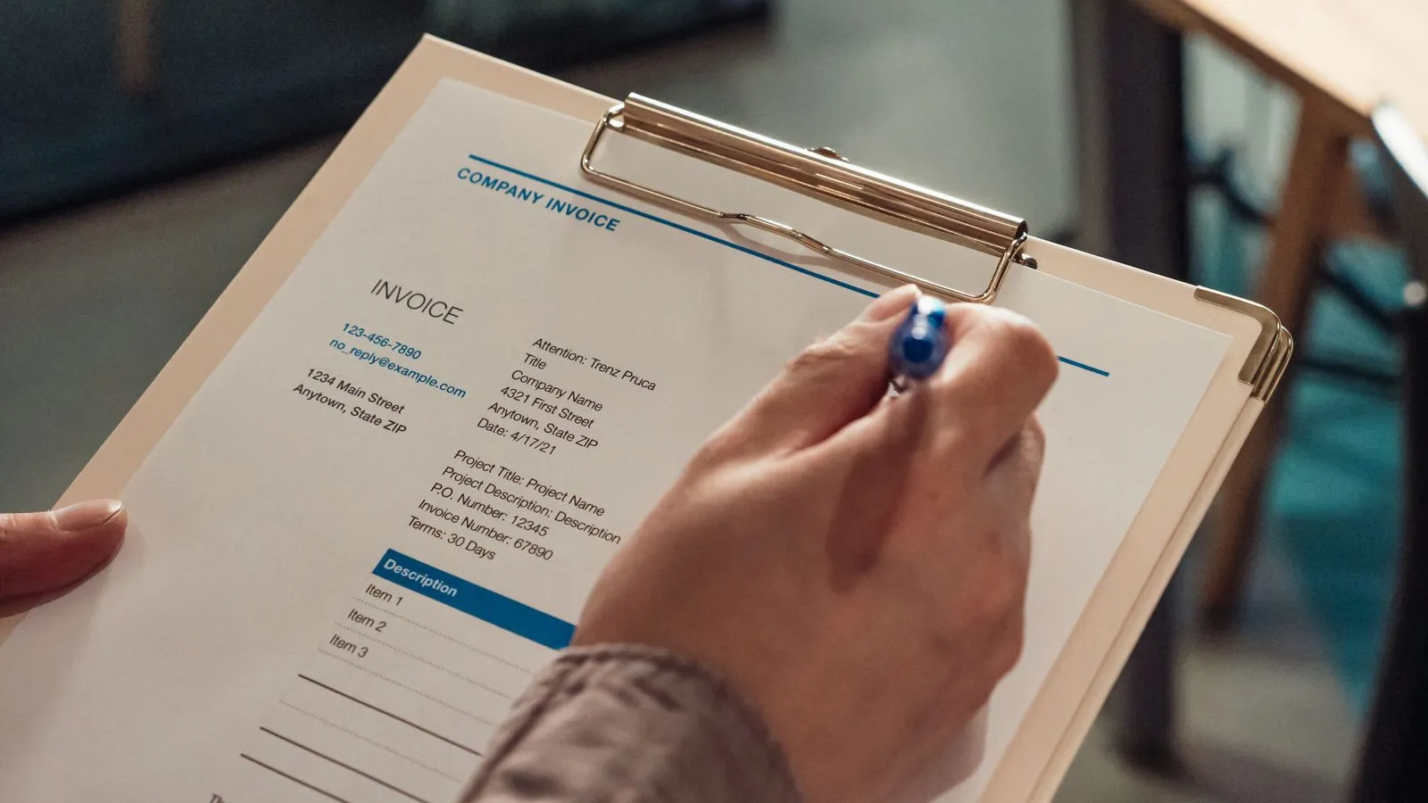 A hand filling in an invoice on a clipboard