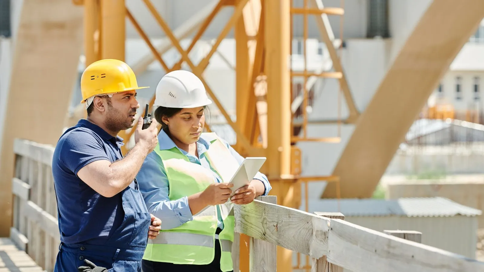 Two people on a job site, one on a radio and one checking a tablet